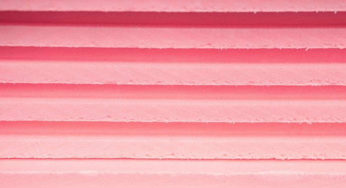 Background soft sheets of foam insulation lie on each other with lines of different shades of pink and purple.