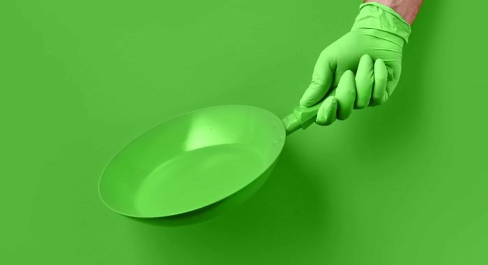 Colored pan in the hand. Chef's hand in glove is holding a green pan on a colored background. Colored pan isolated. Cooking food concepts