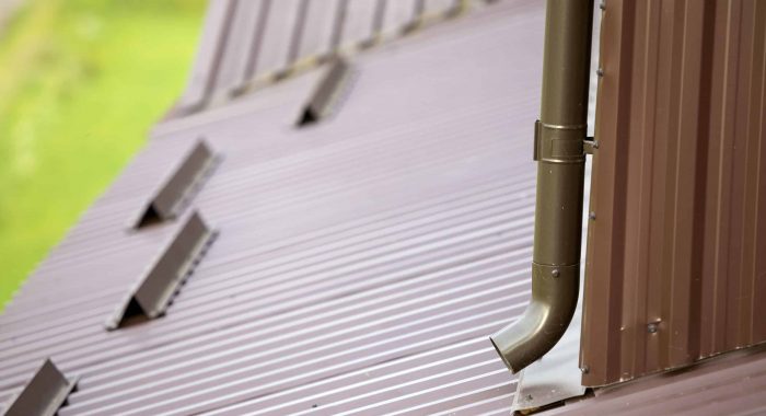 Close-up of brown new gutter metal system pipe on blurred copy space background. Vertical construction for draining rain water from building roof on the wall. Drain protection, professional work.