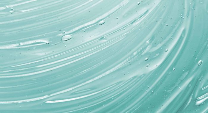 Serum, liquid gel texture. Clear cosmetic cream background. Transpatent mint colored skincare product smudge