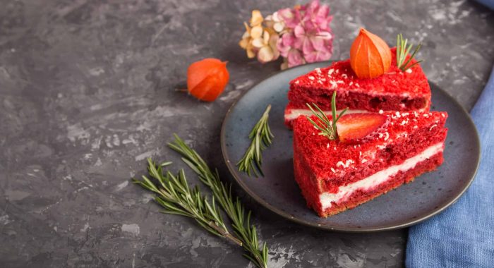 Homemade red velvet cake with milk cream and strawberry on a black concrete background with blue textile. side view, selective focus, copy space.