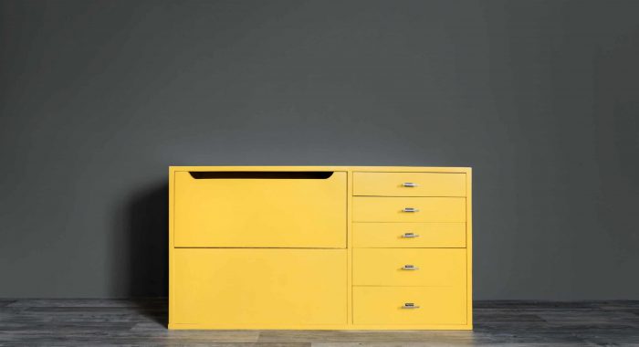 Bright yellow vintage chest of drawers in the room near a dark gray wall.