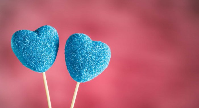 Marmalade in sugar blue in the form of hearts on sticks on a light pink background closeup with copyspace. Valentine's day holiday concept.