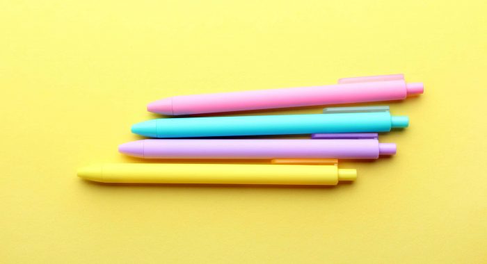 Yellow,purple,blue and pink pens on yellow background. Top view, flat lay.
