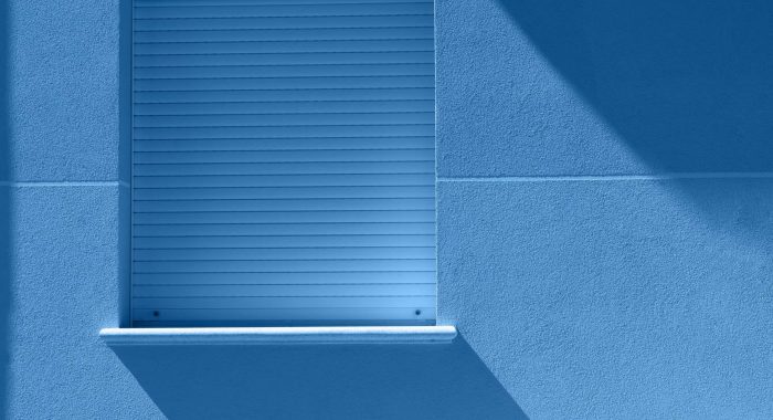 Trendy color of the year 2020. Minimalist blue window with shadow from the sun on a wall. A square blue window hanging on a side wall of house.