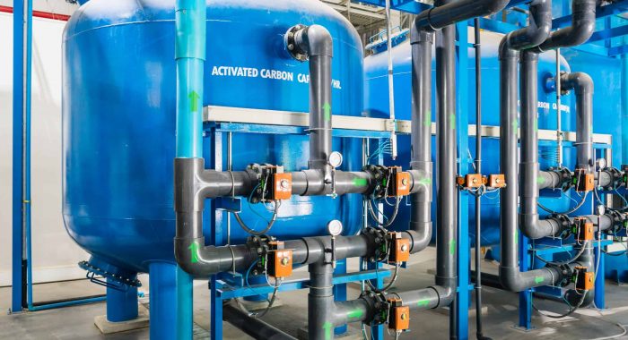 Large industrial water treatment and boiler room. Shiny steel metal pipes and blue pumps and valves.