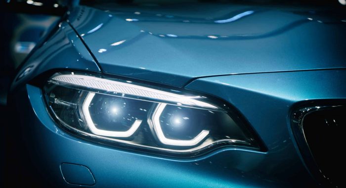 Car headlight and hood of powerful sports blue car with blue glare on dark background. Close up at Car headlight.