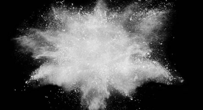Freeze motion explosion of white dust on  black background. By throwing talcum powder out of hand. Stopping the movement of white powder on dark background.